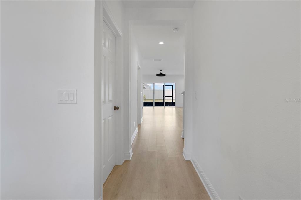 A bright hallway with light wood-look flooring leads toward a glass sliding door — 7781 MARSALA STREET, CLERMONT, FL