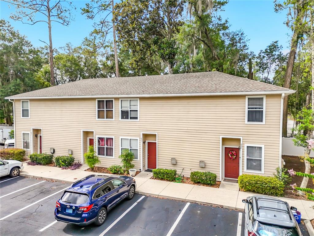 A two-story tan siding apartment building features three red front doors and a parking lot — 1710 NW 7TH STREET UNIT 604, GAINESVILLE, FL