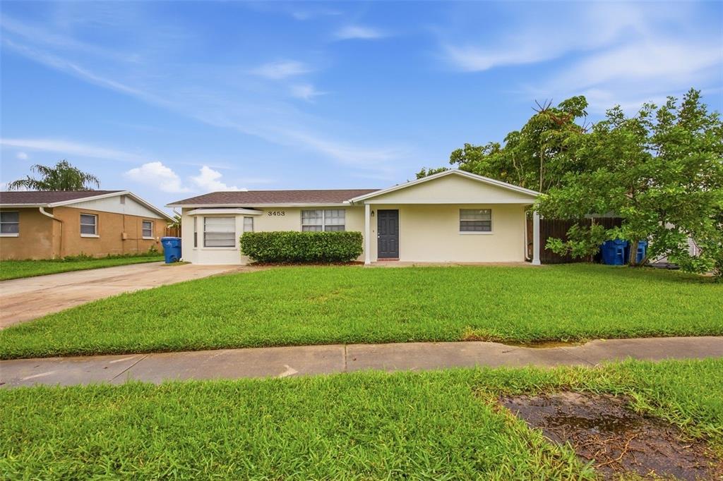 A single-story house with a light-colored exterior, a front lawn, and a dark front door — 3453 WILSON DRIVE, HOLIDAY, FL