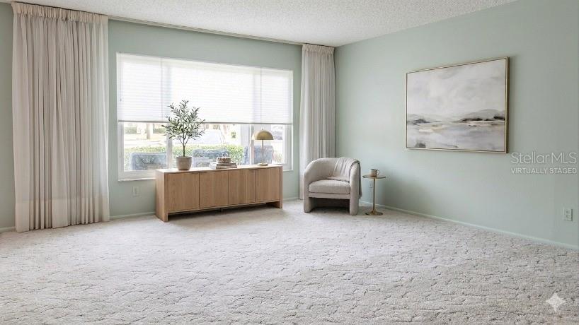 A living room features light green walls, beige carpeting, a wooden console, and an armchair — 2229 AMERICUS BOULEVARD W UNIT 7, CLEARWATER, FL