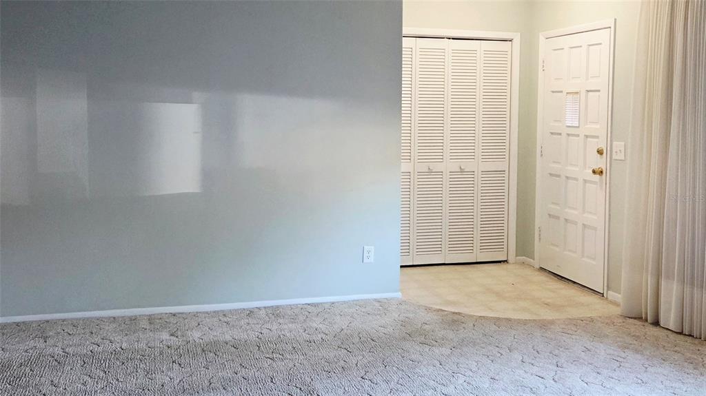 A carpeted room features a large light-colored wall, a white louvered closet, and an entryway — 2229 AMERICUS BOULEVARD W UNIT 7, CLEARWATER, FL