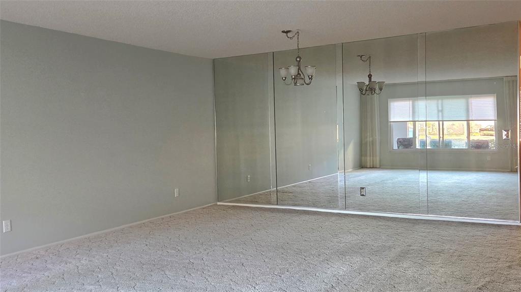 A carpeted living room features a large mirrored wall and a hanging light fixture — 2229 AMERICUS BOULEVARD W UNIT 7, CLEARWATER, FL