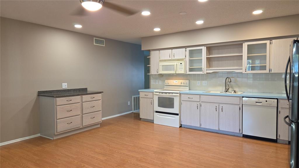 A kitchen features light wood cabinets, white appliances, a dark countertop, and light wood flooring — 2229 AMERICUS BOULEVARD W UNIT 7, CLEARWATER, FL