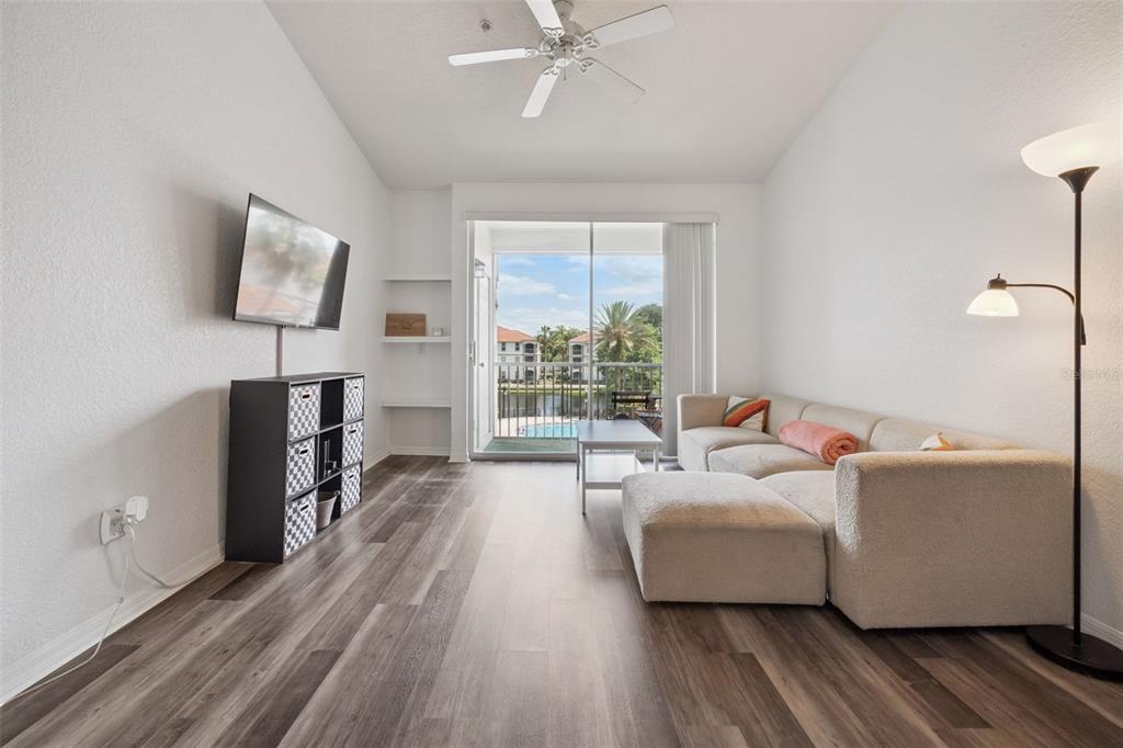 A living room features wood-look flooring, a sectional sofa, a wall-mounted television, and balcony access — 2513 MAITLAND CROSSING WAY UNIT 304, ORLANDO, FL