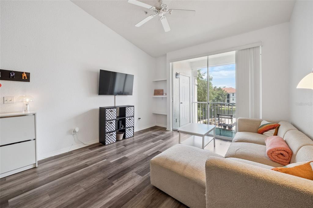 A living room features wood-look flooring, a wall-mounted television, a sectional sofa, and a balcony — 2513 MAITLAND CROSSING WAY UNIT 304, ORLANDO, FL