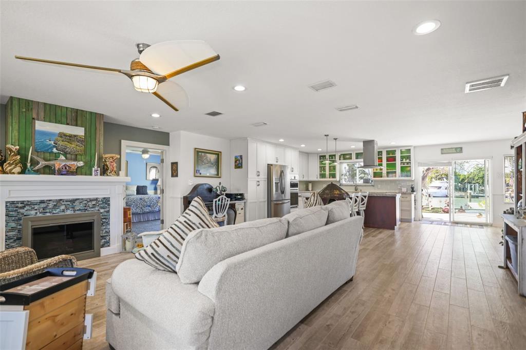 An open-concept living room features a fireplace, a large sofa, and a kitchen with wood-look flooring — 600 NORMANDY ROAD, MADEIRA BEACH, FL