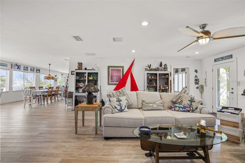 A bright living room features a beige sofa, glass coffee table, and adjacent dining area — 600 NORMANDY ROAD, MADEIRA BEACH, FL