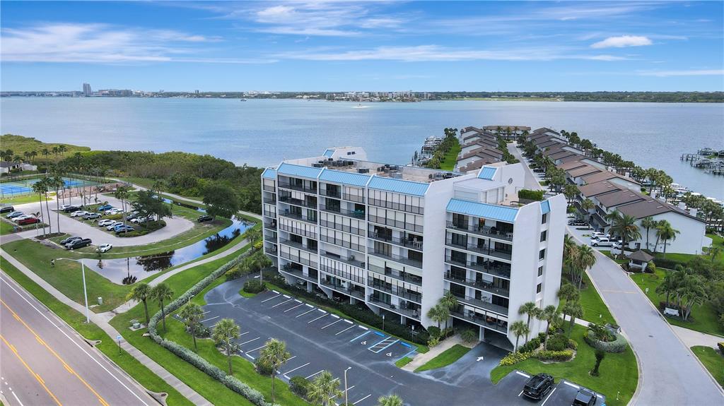An aerial view shows a multi-story apartment building situated near a large body of water — 1581 GULF BOULEVARD UNIT 302N, CLEARWATER BEACH, FL