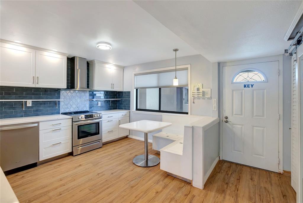 A kitchen features white cabinets, stainless steel appliances, a blue tiled backsplash, and a breakfast nook — 1581 GULF BOULEVARD UNIT 302N, CLEARWATER BEACH, FL