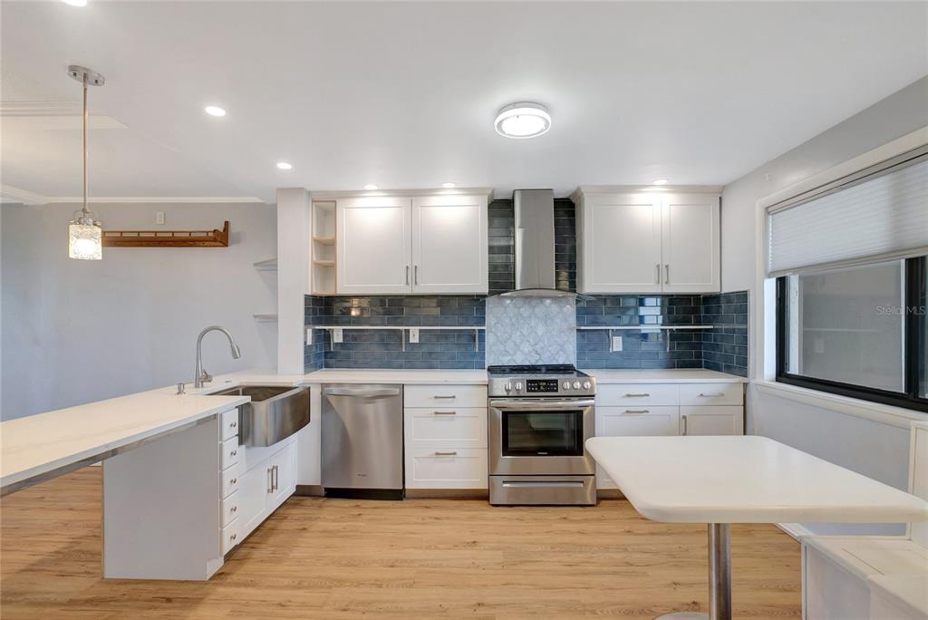 A kitchen features white cabinets, stainless steel appliances, a farmhouse sink, and blue tile backsplash — 1581 GULF BOULEVARD UNIT 302N, CLEARWATER BEACH, FL