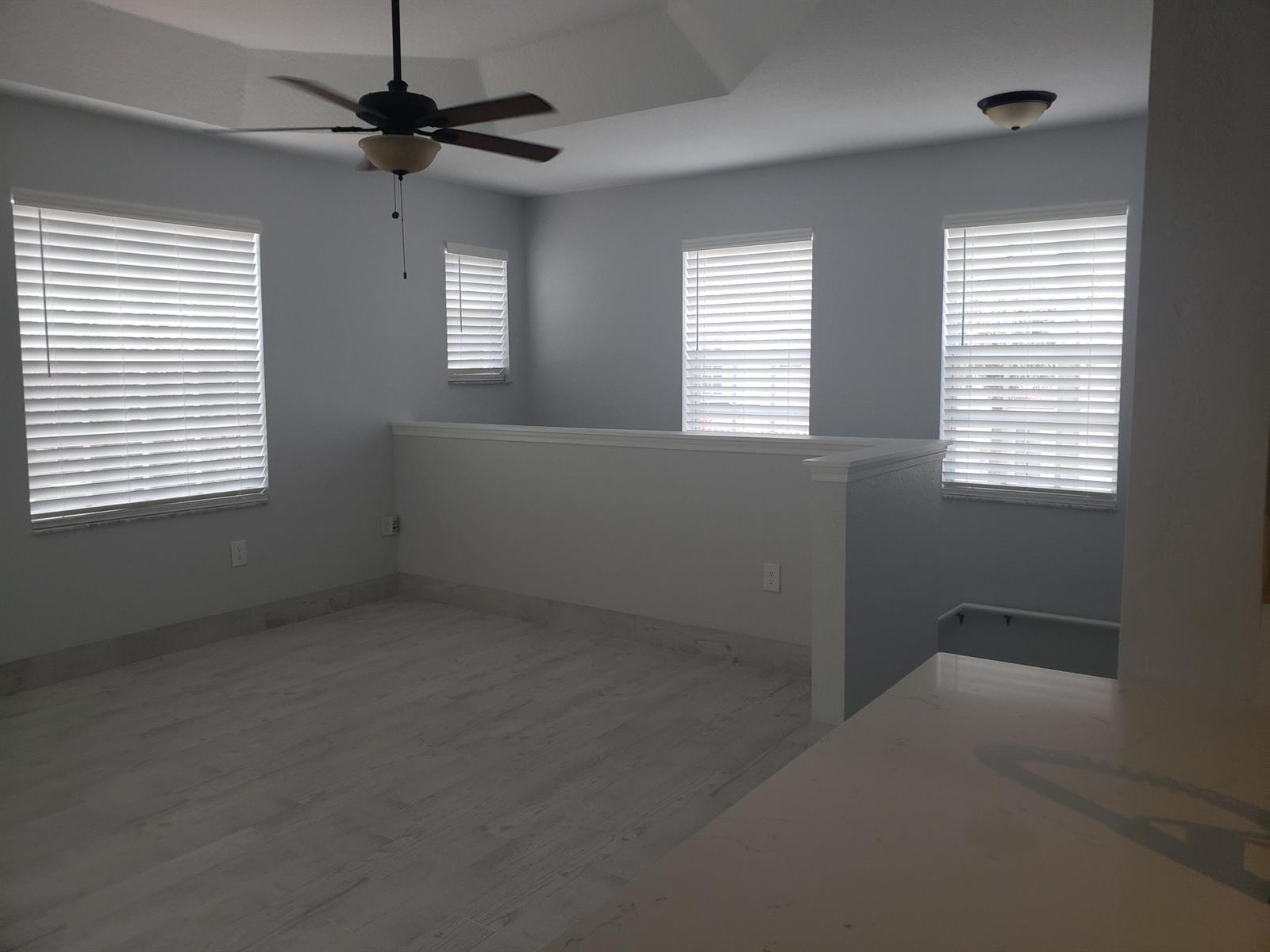 An open loft area with light-colored wood-look flooring, a ceiling fan, and multiple windows — 1005 Belmont Place # 1005, Boynton Beach FL 33436, BOYNTON BEACH, FL