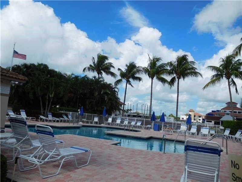 A swimming pool surrounded by lounge chairs, palm trees, and a white fence under blue skies — 6584 Via Regina, Boca Raton FL 33433, BOCA RATON, FL
