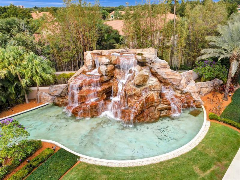 An aerial view of a large rock waterfall feature flowing into a turquoise swimming pool — 6584 Via Regina, Boca Raton FL 33433, BOCA RATON, FL