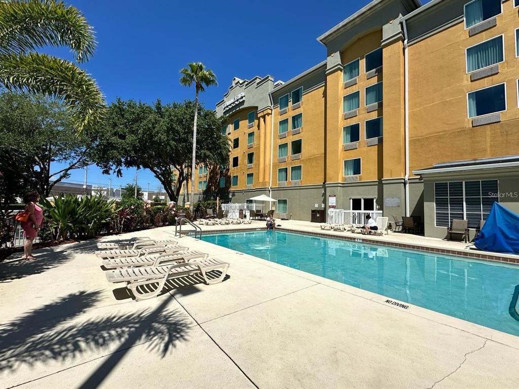 A swimming pool sits in front of a multi-story hotel building under a clear sky — 3000 MAINGATE LANE UNIT 326, KISSIMMEE, FL