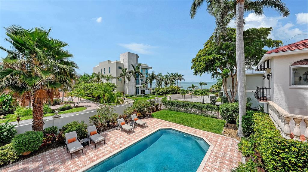 A backyard features a swimming pool, patio furniture, and palm trees overlooking a bay — 1023 TOCOBAGA LANE, SARASOTA, FL