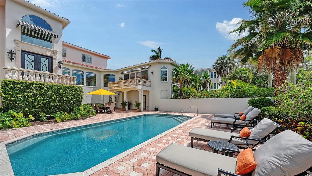 A swimming pool sits in a backyard patio area with lounge chairs and a house — 1023 TOCOBAGA LANE, SARASOTA, FL