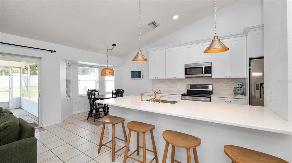 A kitchen features white cabinets, a quartz island with bar stools, and a dining area — 3045 LILLIAN PASS, LAKELAND, FL