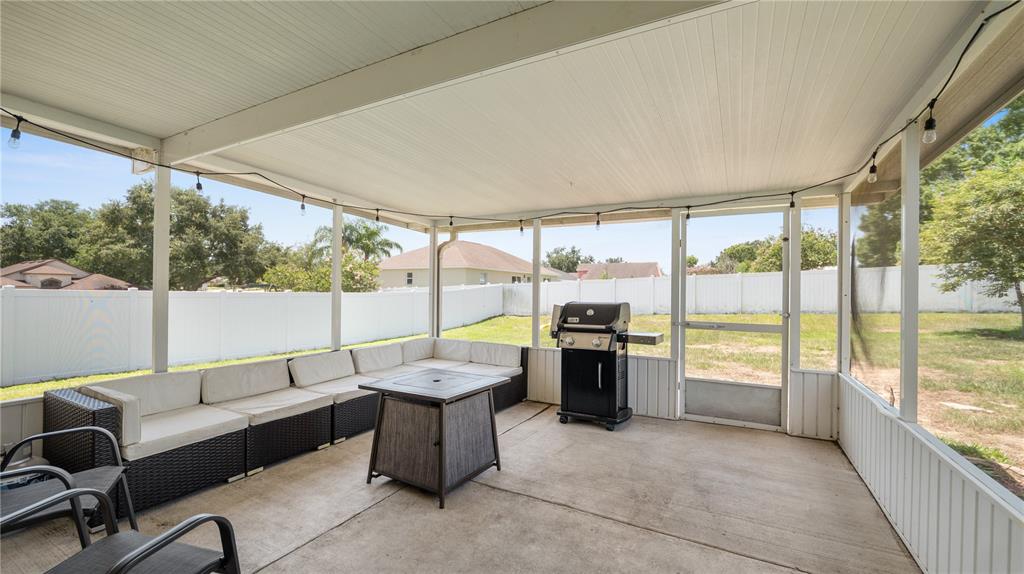A screened-in patio features a concrete floor, modular outdoor seating, a grill, and string lights — 3045 LILLIAN PASS, LAKELAND, FL
