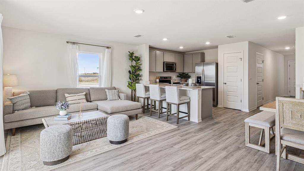An open-concept living room and kitchen feature gray cabinetry, stainless appliances, and wood-look flooring — 4702 TONY STREET, LAKE WALES, FL