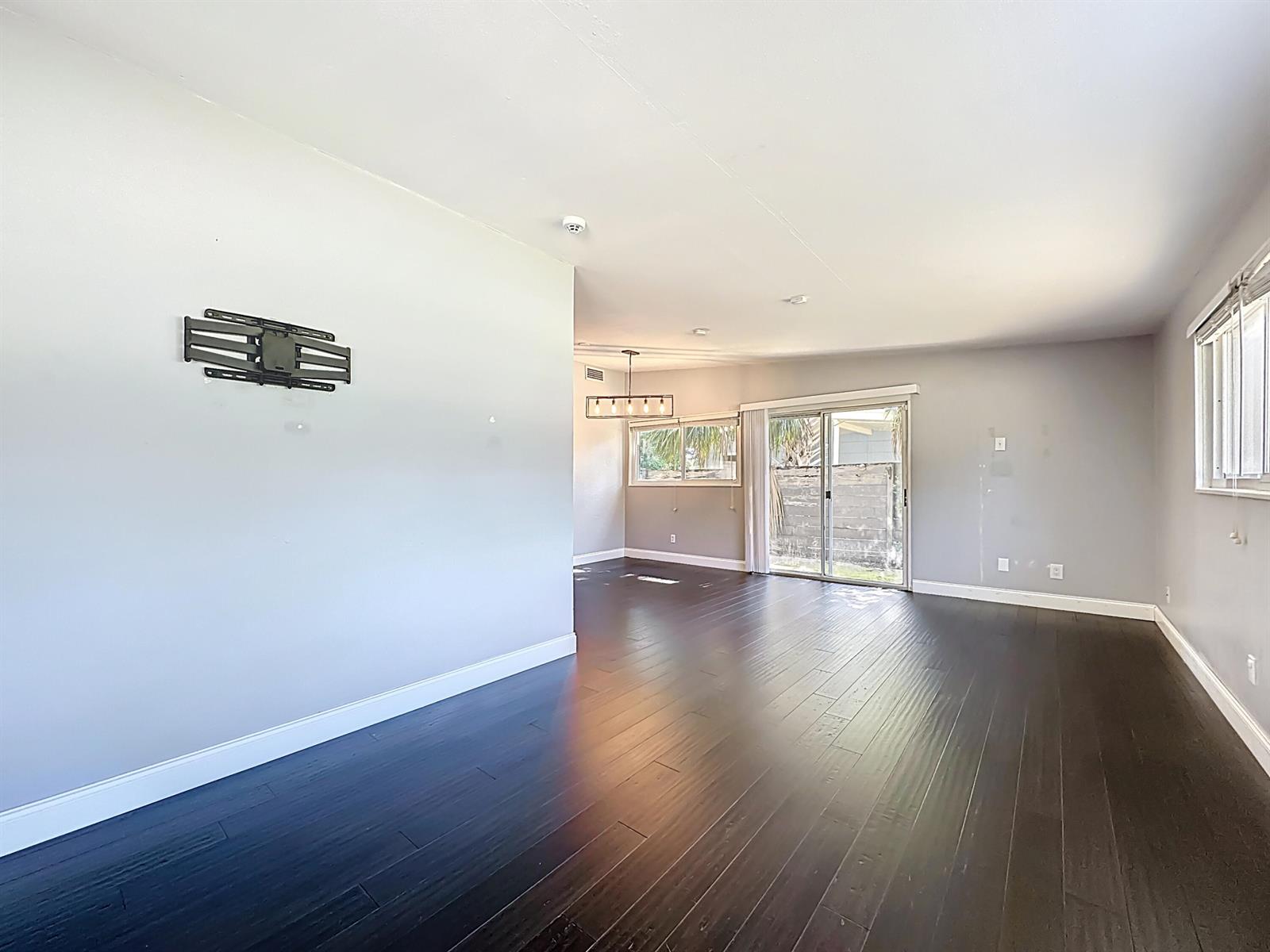 An empty living room features dark hardwood floors, light gray walls, and a sliding glass door — 7615 Mayapple Road, Jacksonville FL 32211, JACKSONVILLE, FL