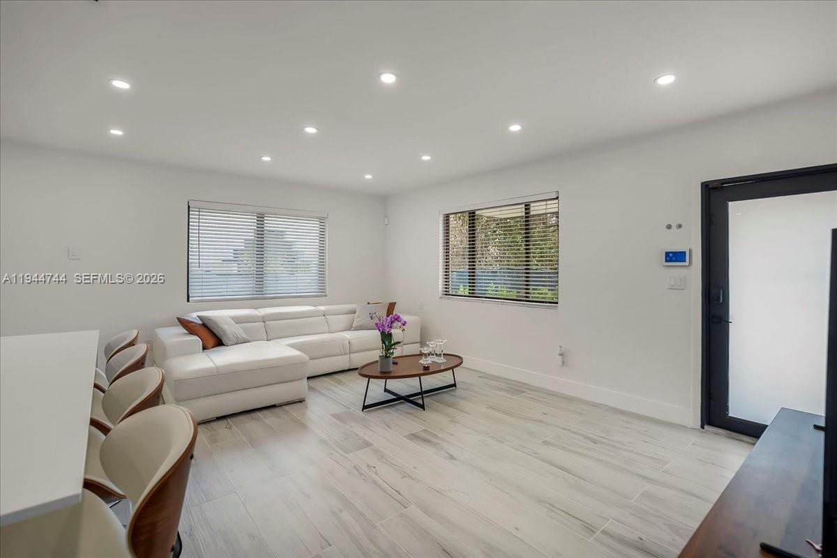 A living room features white walls, light wood-look flooring, a white sectional, and recessed lighting — 70 NW 47th Ter, Miami FL 33127, MIAMI, FL
