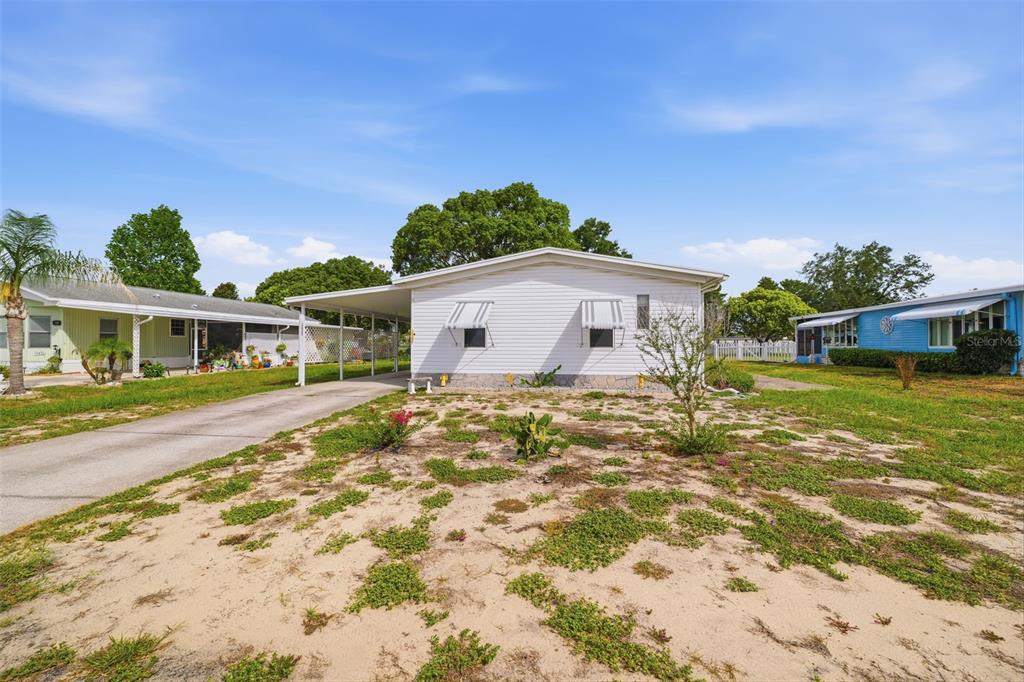 A white single-story manufactured home features a carport and a sandy front yard — 15439 BROOKRIDGE BOULEVARD, BROOKSVILLE, FL