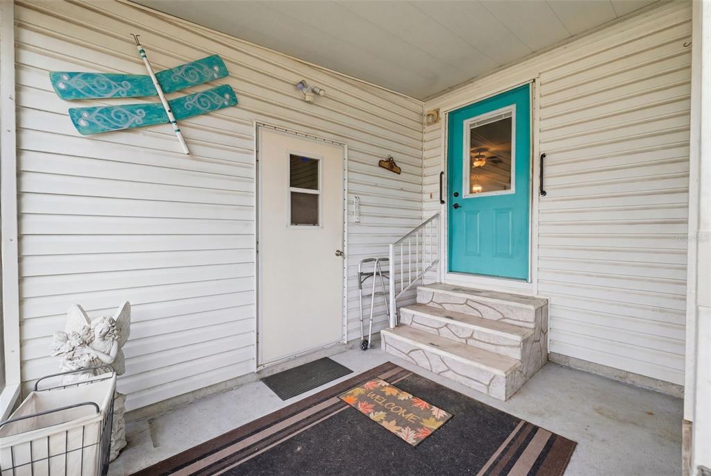 A covered porch features white siding, a teal front door, and a decorative dragonfly wall hanging — 15439 BROOKRIDGE BOULEVARD, BROOKSVILLE, FL