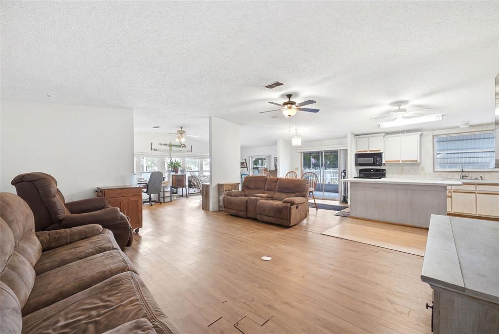 An open-concept living room and kitchen featuring wood-look flooring, brown furniture, and ceiling fans — 15439 BROOKRIDGE BOULEVARD, BROOKSVILLE, FL