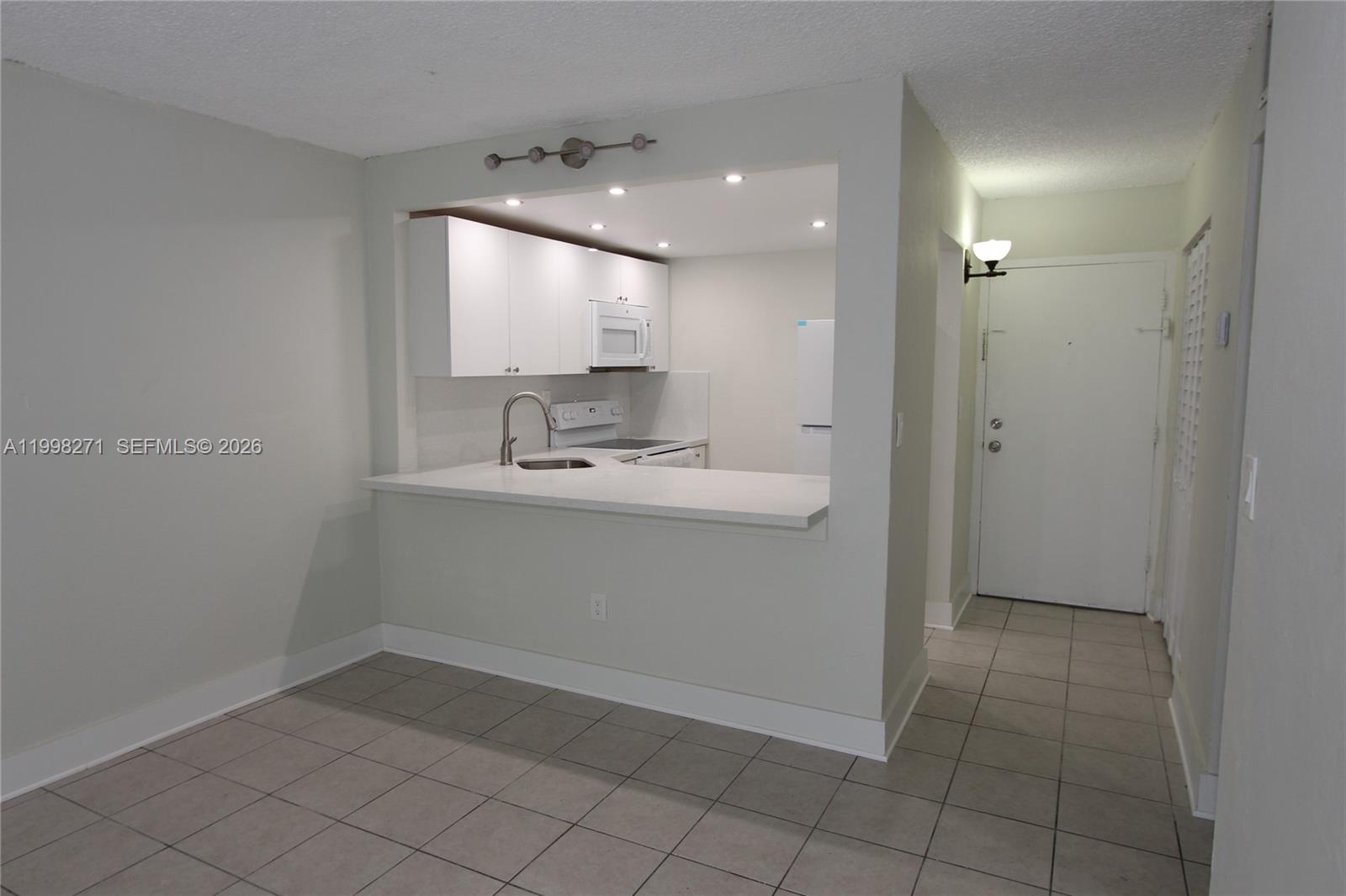 A kitchen with white cabinets and a breakfast bar opens into a tiled living area — 4550 NW 9th St # 811E, Miami FL 33126, MIAMI, FL