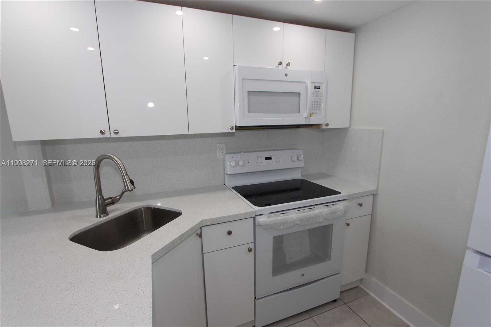 A compact kitchen features white cabinets, a stainless steel sink, and white appliances — 4550 NW 9th St # 811E, Miami FL 33126, MIAMI, FL