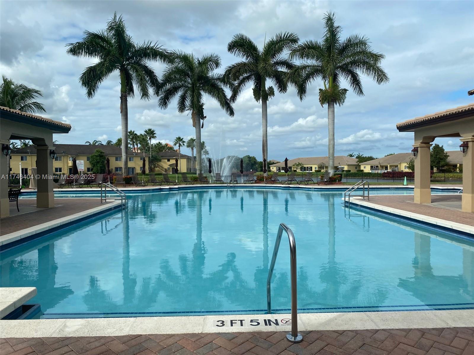 A swimming pool with a fountain and palm trees is surrounded by a paved deck — 1420 NE 33rd Ave # 15, Homestead FL 33033, HOMESTEAD, FL