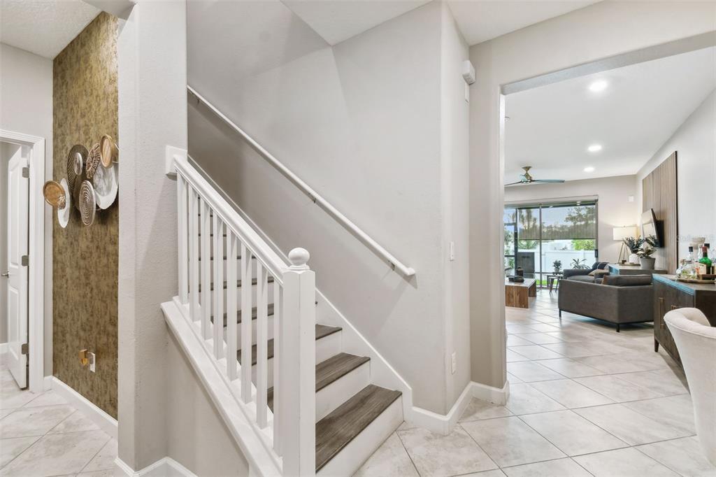 A staircase with wood-look treads and white railings sits beside a tiled living area — 10012 CORSO MILANO DRIVE, TAMPA, FL