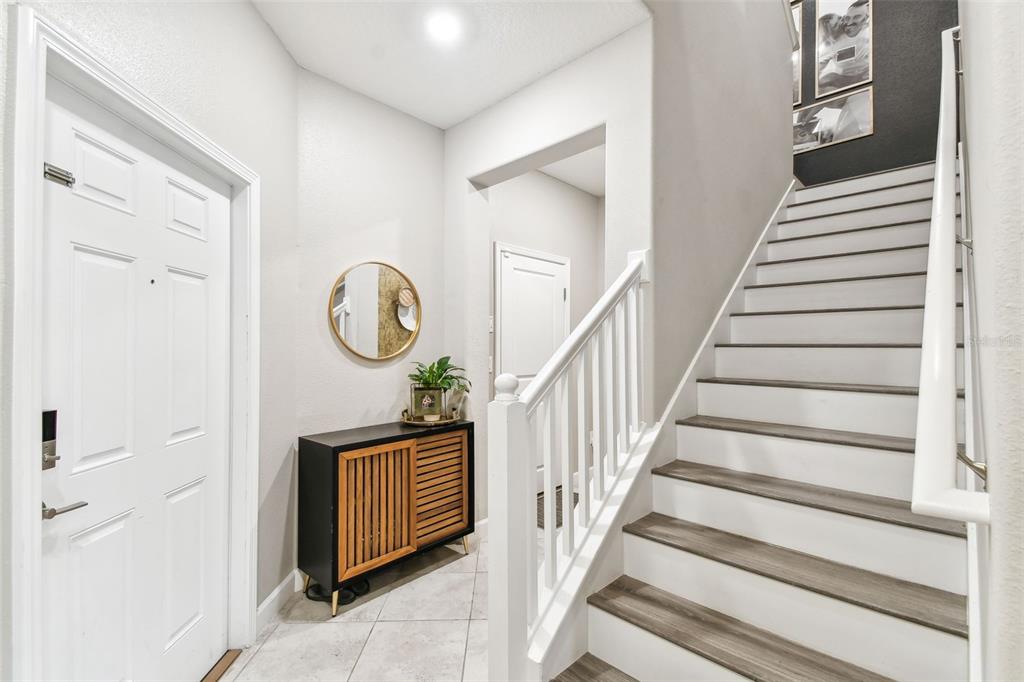 An entryway features a white front door, a wooden cabinet, and stairs with white railings — 10012 CORSO MILANO DRIVE, TAMPA, FL