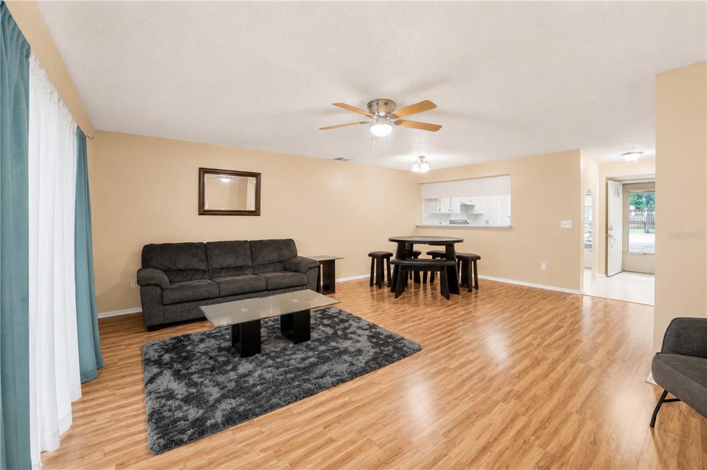 A living room with wood-look flooring, a gray sofa, a glass coffee table, and dining area — 602 SAINT HENRY DRIVE, BRANDON, FL