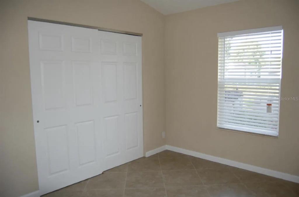 A bedroom with beige walls, tile flooring, a white sliding closet door, and a window — 926 SW 11TH TERRACE, DELRAY BEACH, FL