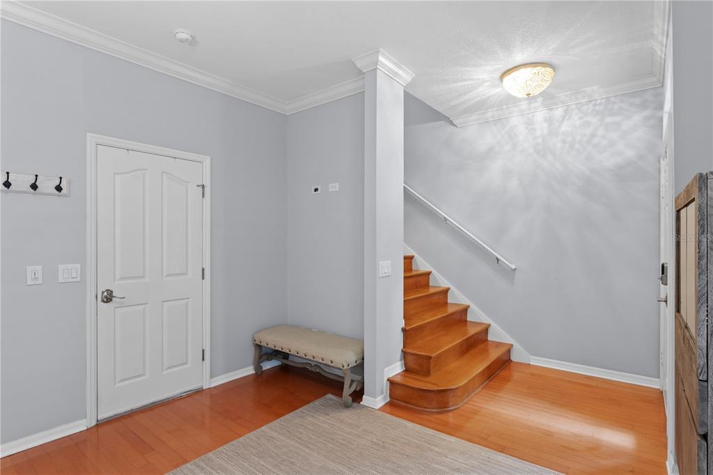 An entryway features hardwood floors, a wooden staircase, a beige bench, and a white door — 1425 HARBOUR WALK ROAD, TAMPA, FL