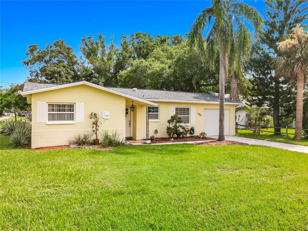 A single-story yellow house with a white garage, a front lawn, and palm trees — 105 JUDY LEE DRIVE, LARGO, FL