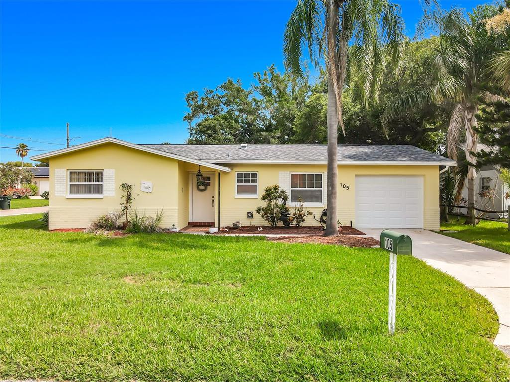 A yellow single-story house with a white garage door, a front lawn, and a palm tree — 105 JUDY LEE DRIVE, LARGO, FL