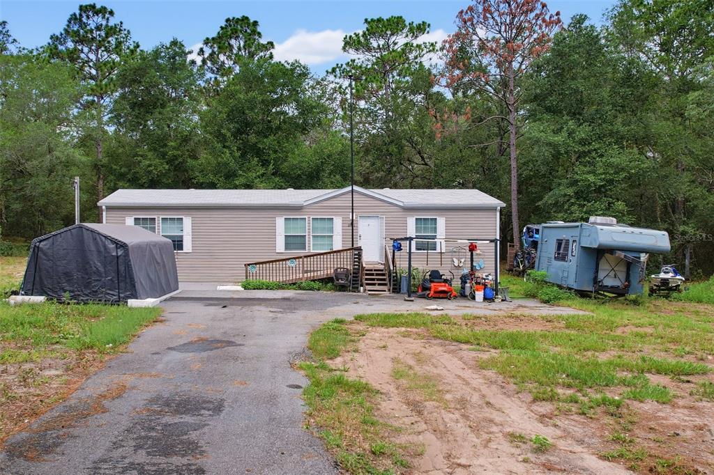 A single-story manufactured home with a driveway, a portable garage, and a parked trailer — 17721 DRAYTON STREET, SPRING HILL, FL