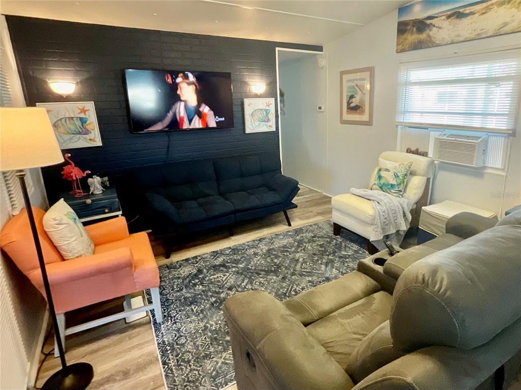 A living room features a dark brick accent wall with a television and varied seating — 6580 SEMINOLE BOULEVARD UNIT 510, SEMINOLE, FL