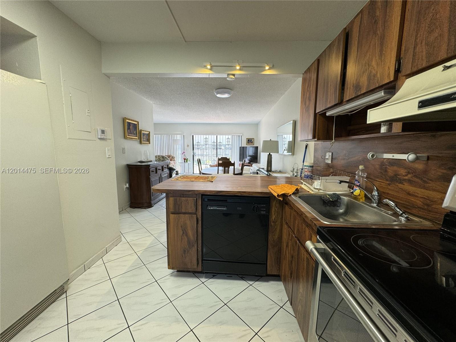 A kitchen with wood cabinets and a black dishwasher overlooks a living and dining area — 3817 SW 82nd Ave # 46, Miami FL 33155, MIAMI, FL