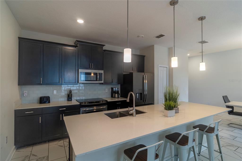 A modern kitchen features dark cabinetry, a large quartz-topped island, and stainless steel appliances — 436 OCEAN COURSE AVENUE, DAVENPORT, FL