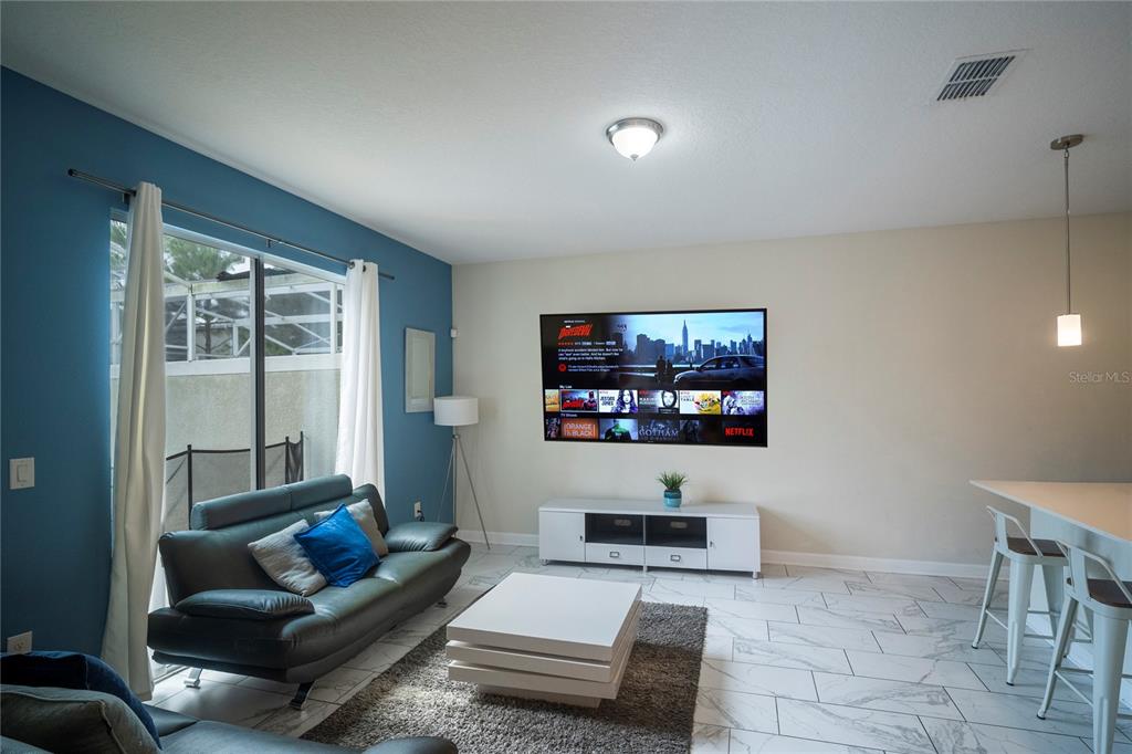 A living room features a blue accent wall, a wall-mounted television, and white tile flooring — 436 OCEAN COURSE AVENUE, DAVENPORT, FL