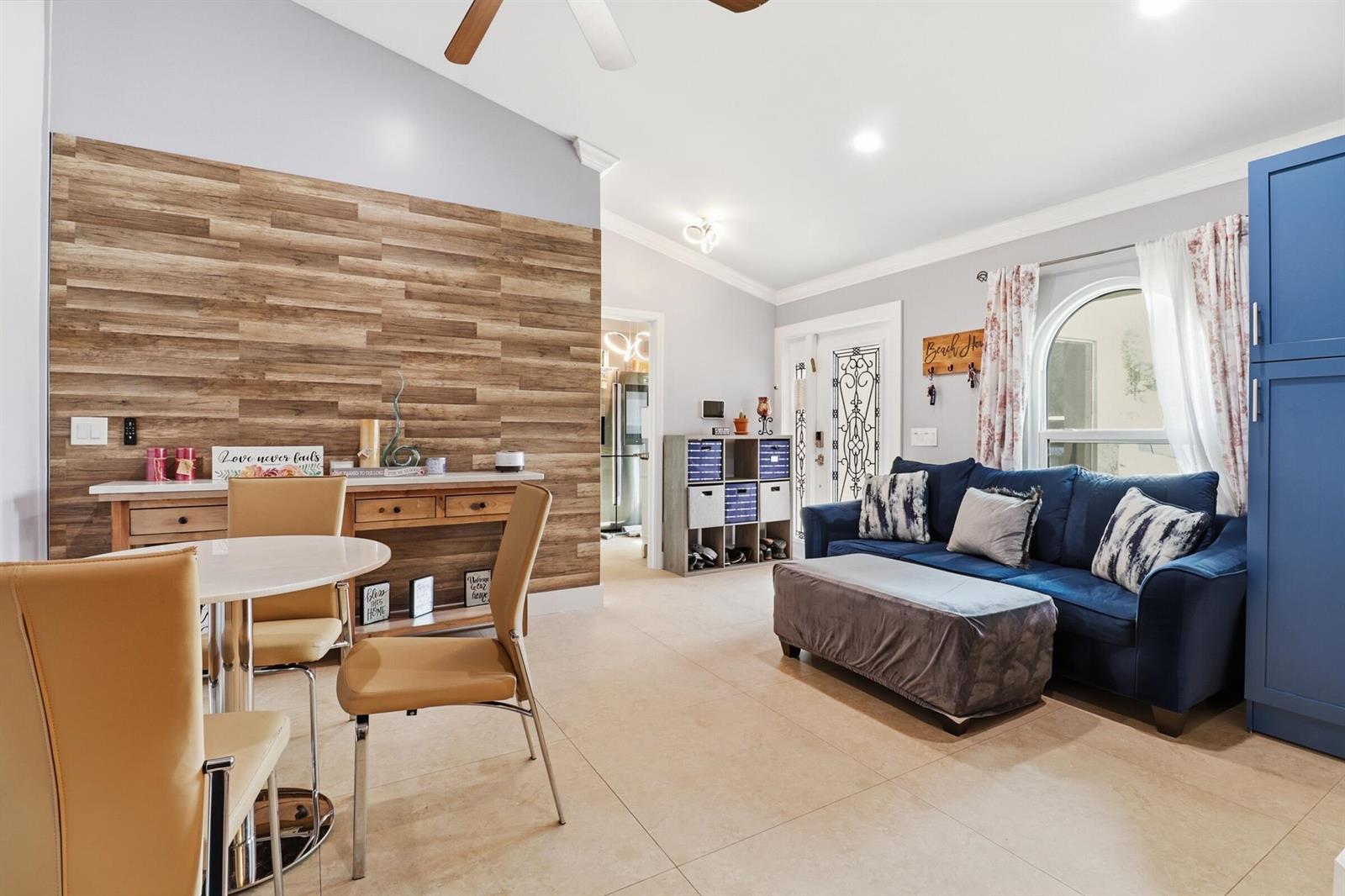 A living and dining area features a wood-paneled accent wall, tile flooring, and blue furniture — 1424 Primrose Lane, Wellington FL 33414, WELLINGTON, FL