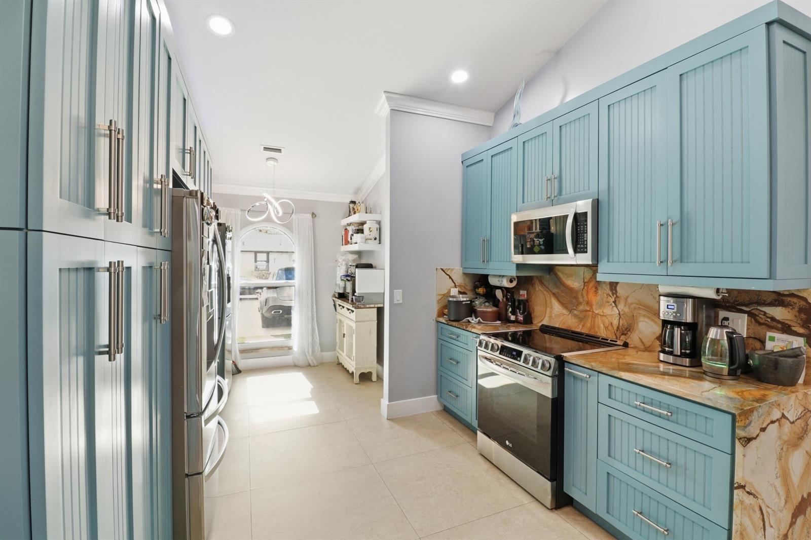 A kitchen features blue beadboard cabinets, a stone backsplash, and stainless steel appliances — 1424 Primrose Lane, Wellington FL 33414, WELLINGTON, FL