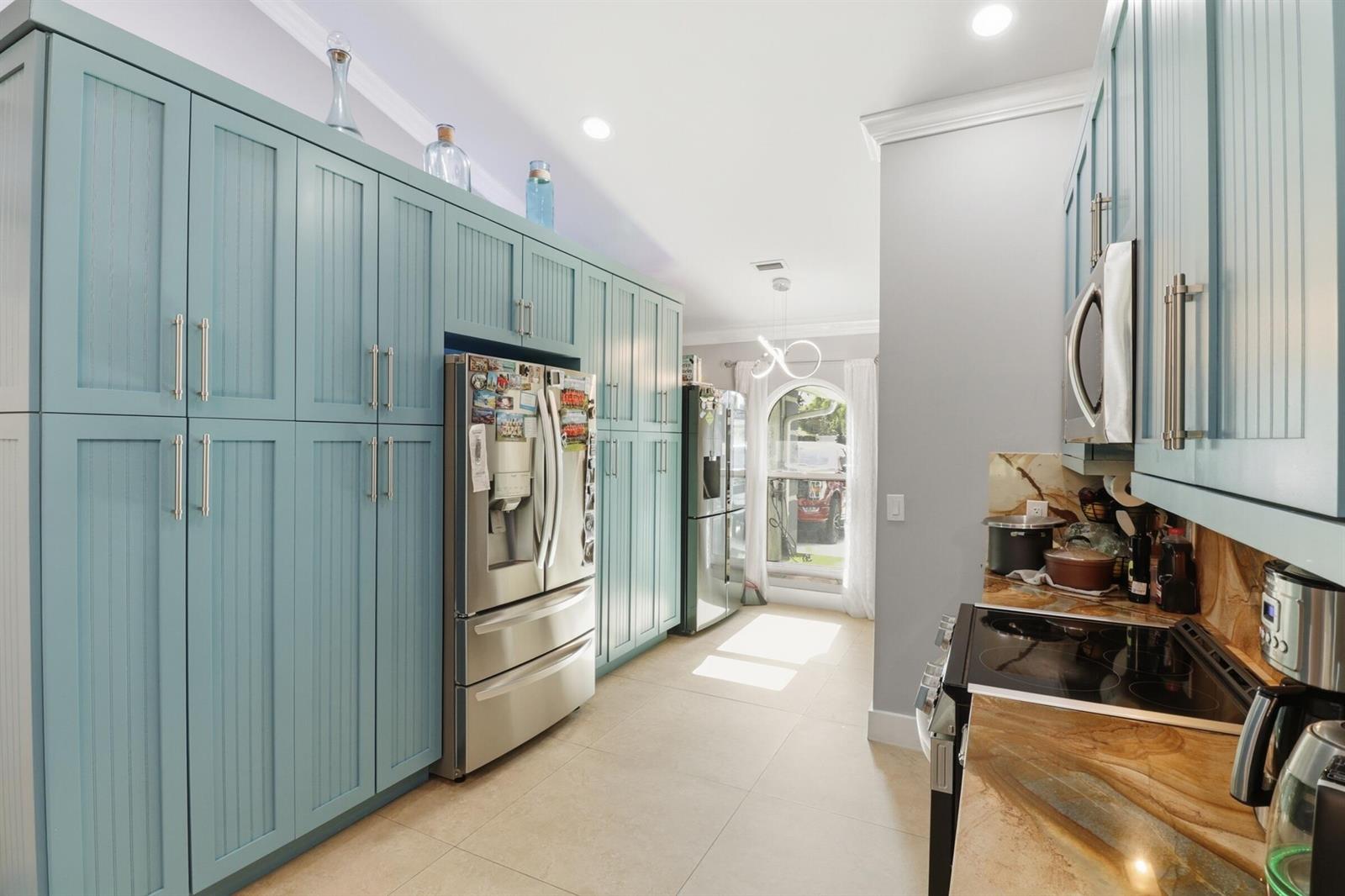 A kitchen features light blue cabinetry, stainless steel appliances, and brown marble countertops — 1424 Primrose Lane, Wellington FL 33414, WELLINGTON, FL