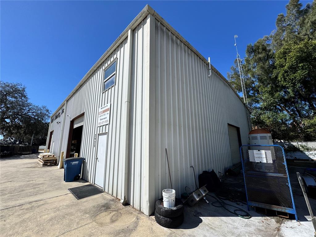 An exterior view of a metal-sided commercial building with a blue trash bin and equipment — 2914 KENILWORTH BOULEVARD, SEBRING, FL