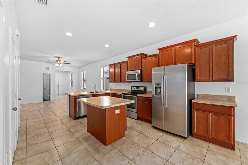 A kitchen features wood cabinets, stainless steel appliances, a center island, and tile flooring — 6308 MAGNOLIA PARK BOULEVARD, RIVERVIEW, FL