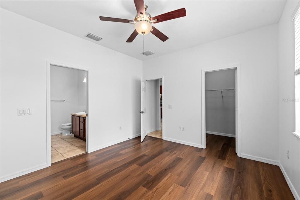 A bedroom with wood-look flooring, a ceiling fan, and doorways leading to a bathroom and closet — 6308 MAGNOLIA PARK BOULEVARD, RIVERVIEW, FL