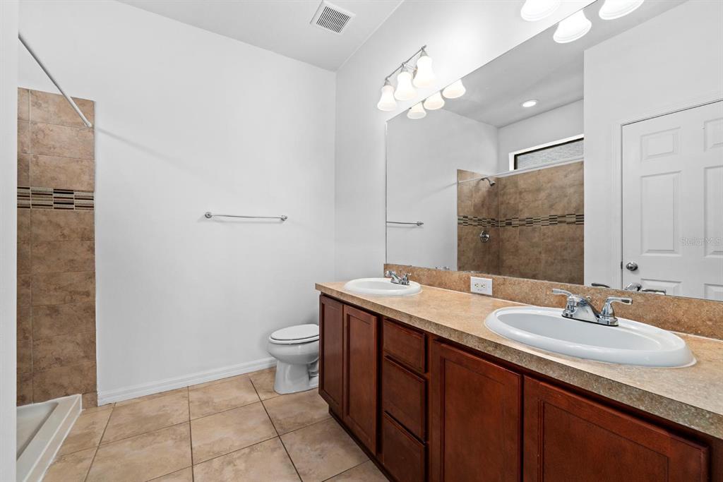 A bathroom features a double vanity with a tan countertop, wood cabinets, and tiled flooring — 6308 MAGNOLIA PARK BOULEVARD, RIVERVIEW, FL